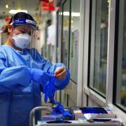 A healthcare worker wearing PPE respirator, face shield, and gown while putting on gloves. Photo: PA